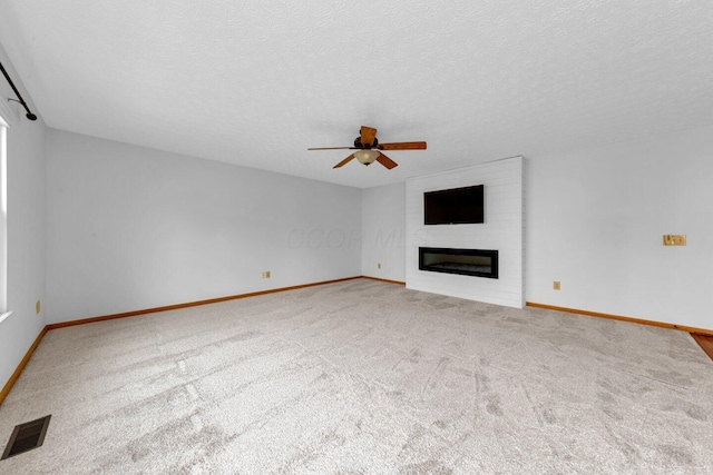 unfurnished living room with ceiling fan, a textured ceiling, a large fireplace, visible vents, and carpet