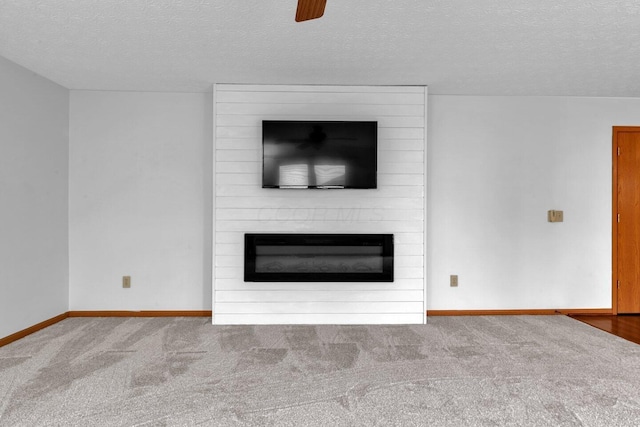 unfurnished living room with carpet floors, a large fireplace, baseboards, and a textured ceiling