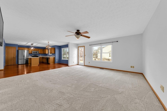 unfurnished living room featuring a textured ceiling, carpet flooring, visible vents, a ceiling fan, and baseboards