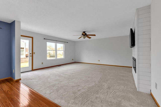 unfurnished living room with a ceiling fan, a fireplace, a textured ceiling, and baseboards