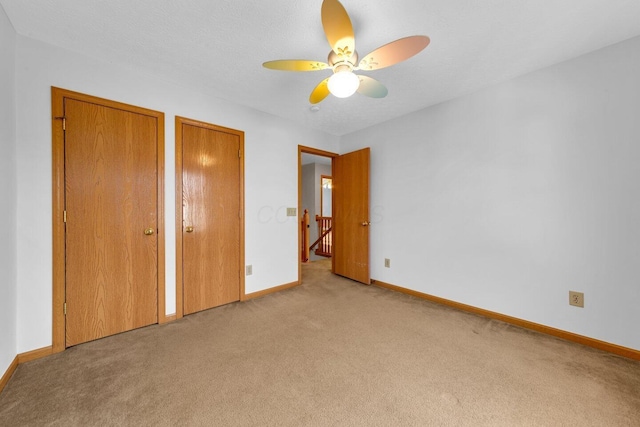 unfurnished bedroom with a textured ceiling, carpet floors, a ceiling fan, baseboards, and two closets