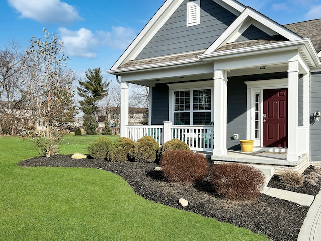 view of front of house with a shingled roof, covered porch, and a front lawn