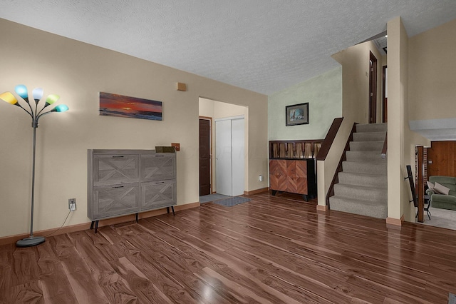 unfurnished living room featuring stairway, vaulted ceiling, a textured ceiling, wood finished floors, and baseboards