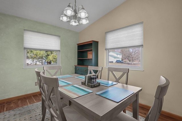 dining area with vaulted ceiling, plenty of natural light, wood finished floors, and an inviting chandelier