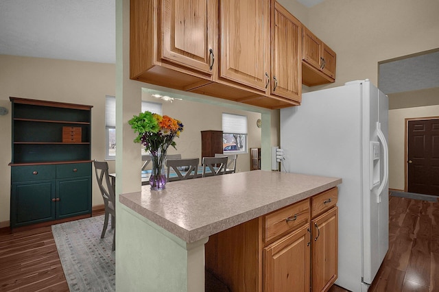 kitchen with a peninsula, white fridge with ice dispenser, light countertops, and dark wood-style flooring