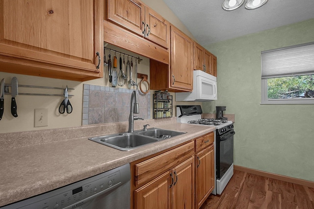 kitchen featuring range with gas stovetop, white microwave, a sink, dishwasher, and baseboards