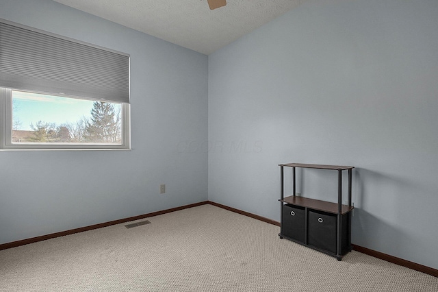 empty room featuring a textured ceiling, light colored carpet, a ceiling fan, baseboards, and visible vents