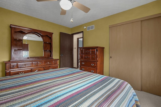 bedroom with visible vents, ceiling fan, a textured ceiling, carpet floors, and a closet