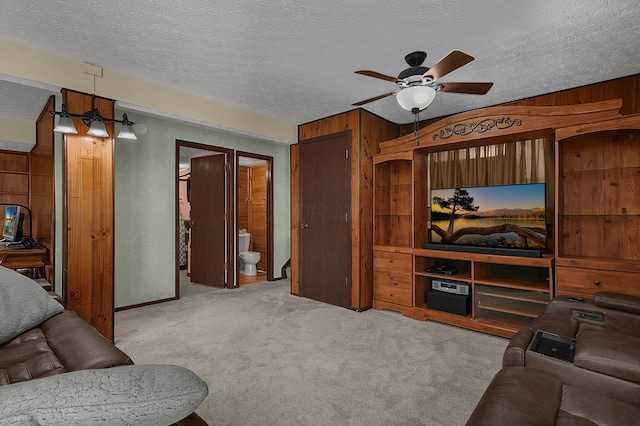 living area featuring carpet floors, ceiling fan, wooden walls, and a textured ceiling