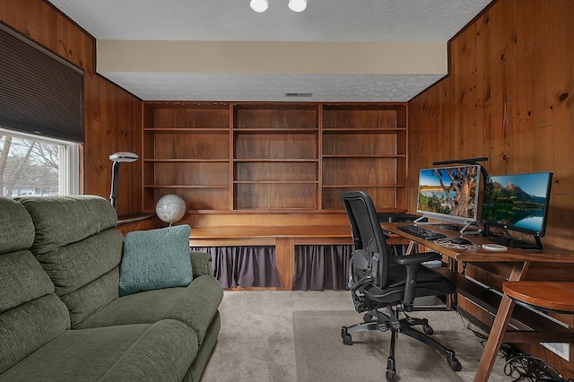 office area with carpet, wooden walls, visible vents, and a textured ceiling