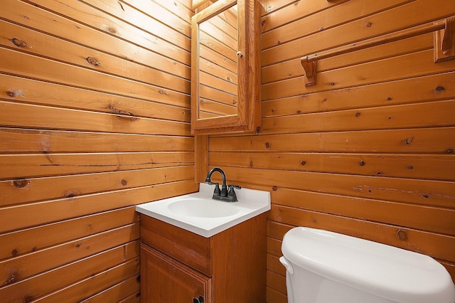 bathroom with toilet, wooden walls, and vanity