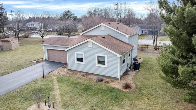 exterior space featuring central AC unit, an attached garage, driveway, roof with shingles, and a front yard