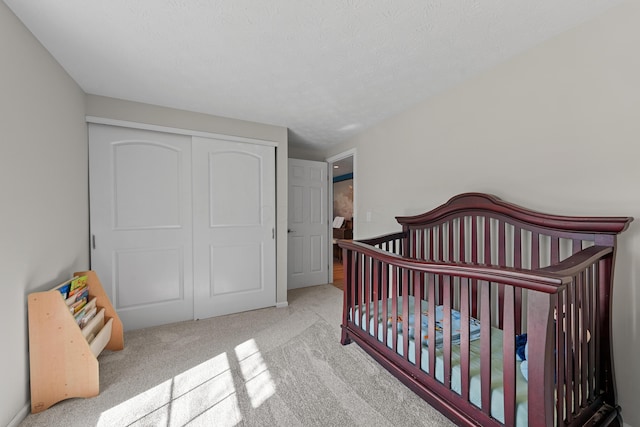 carpeted bedroom featuring a nursery area, a closet, and a textured ceiling