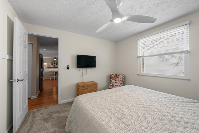 carpeted bedroom with a textured ceiling, baseboards, freestanding refrigerator, and a ceiling fan