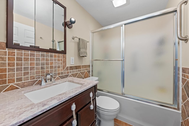 bathroom featuring tile walls, enclosed tub / shower combo, vanity, and toilet