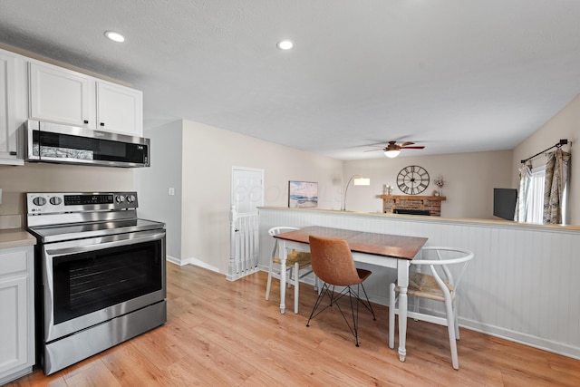 kitchen featuring a fireplace, a ceiling fan, white cabinets, light wood-style floors, and appliances with stainless steel finishes