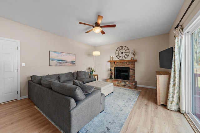 living area featuring a brick fireplace, ceiling fan, light wood-style flooring, and baseboards