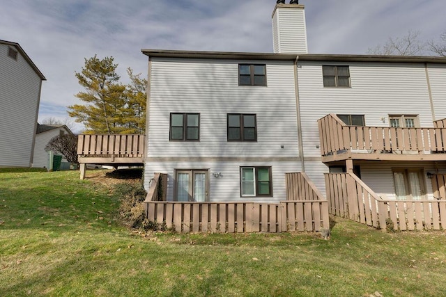 rear view of property with a chimney, a lawn, and a deck