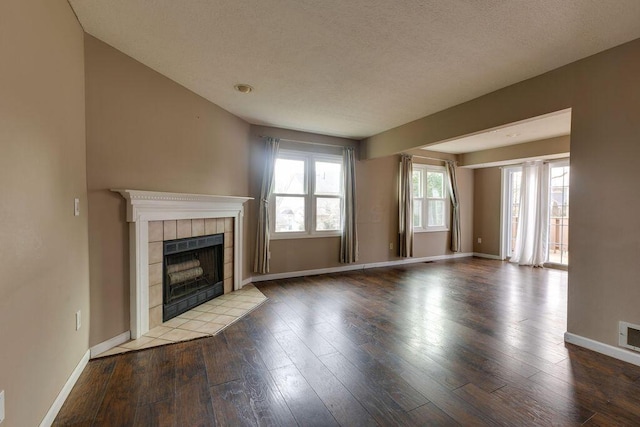 unfurnished living room with a fireplace, a textured ceiling, baseboards, and wood finished floors