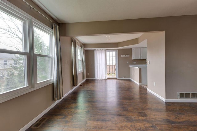 unfurnished living room with dark wood-style flooring, visible vents, and baseboards