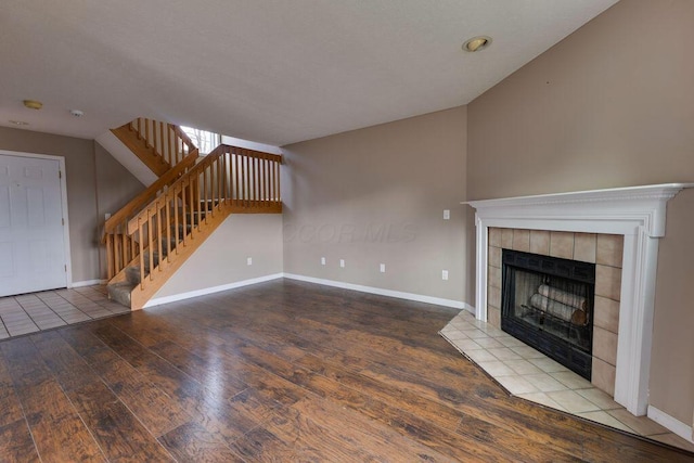 unfurnished living room featuring stairs, a tile fireplace, wood finished floors, and baseboards