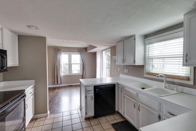 kitchen featuring black appliances, a peninsula, a sink, and light countertops