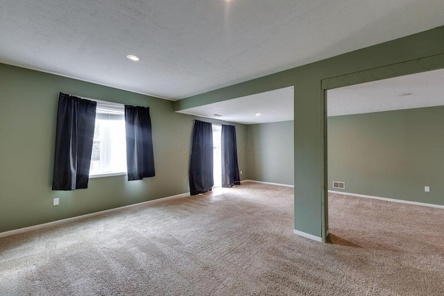 carpeted empty room with visible vents, a textured ceiling, and baseboards