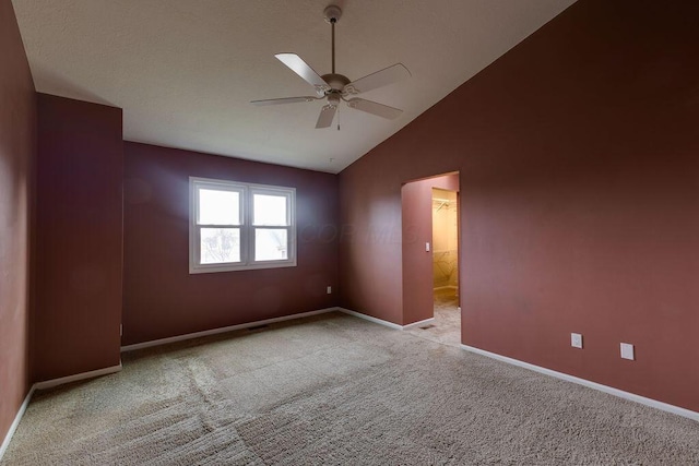 carpeted empty room with vaulted ceiling, a ceiling fan, and baseboards