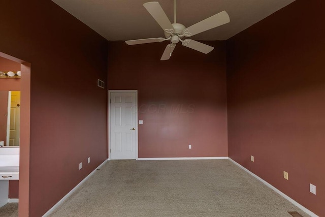 carpeted empty room with a towering ceiling, baseboards, visible vents, and a ceiling fan