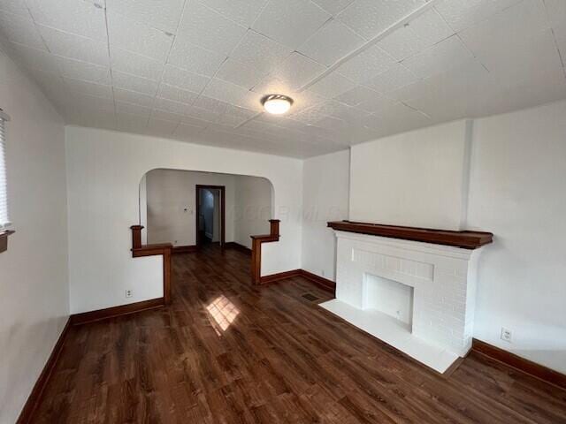 unfurnished living room featuring baseboards, a fireplace, arched walkways, and wood finished floors