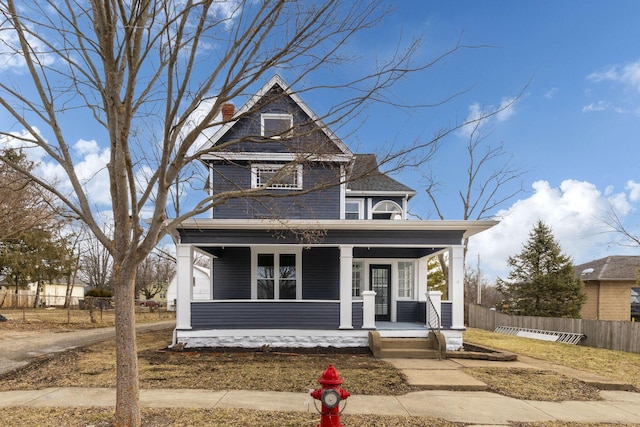 view of front of home with covered porch, fence, and a chimney