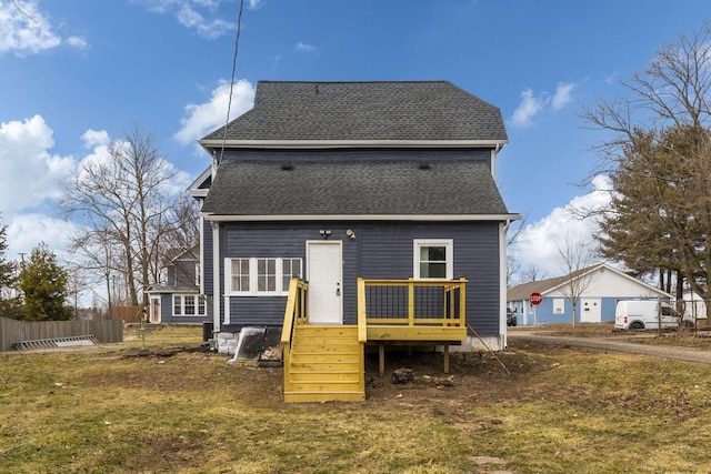 rear view of house featuring a shingled roof, fence, a deck, and a lawn