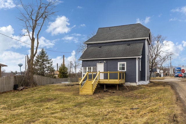 rear view of house with a shingled roof, a lawn, fence, and a wooden deck