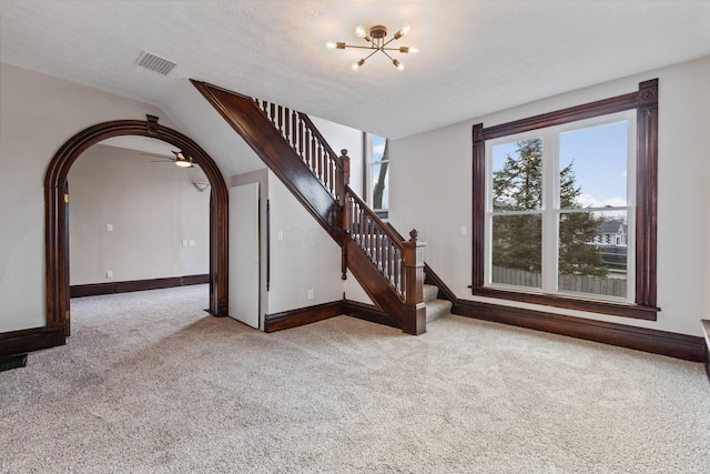 unfurnished living room with arched walkways, visible vents, stairway, carpet, and an inviting chandelier