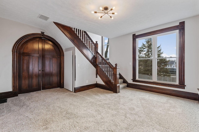 entryway featuring a chandelier, light carpet, visible vents, baseboards, and stairs