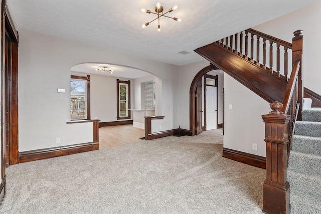 empty room with carpet, arched walkways, visible vents, an inviting chandelier, and stairs