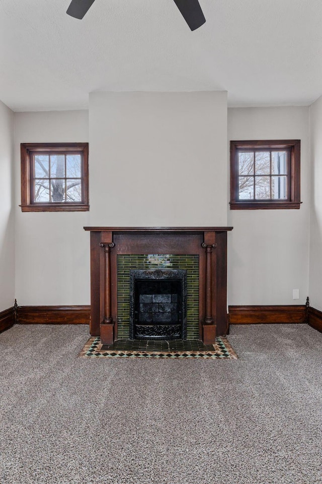 unfurnished living room featuring ceiling fan, a tile fireplace, carpet flooring, and baseboards