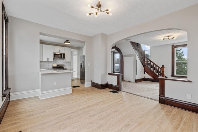 unfurnished living room featuring arched walkways, an inviting chandelier, a textured ceiling, light wood-type flooring, and baseboards