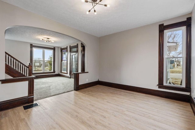 interior space featuring visible vents, arched walkways, stairway, a textured ceiling, and light wood-type flooring