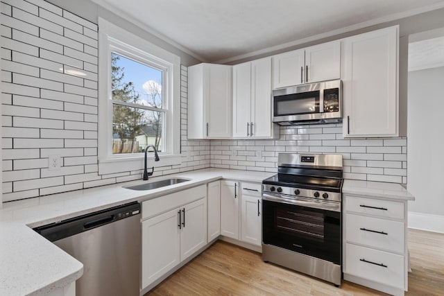 kitchen with stainless steel appliances, white cabinets, a sink, and light wood-style flooring