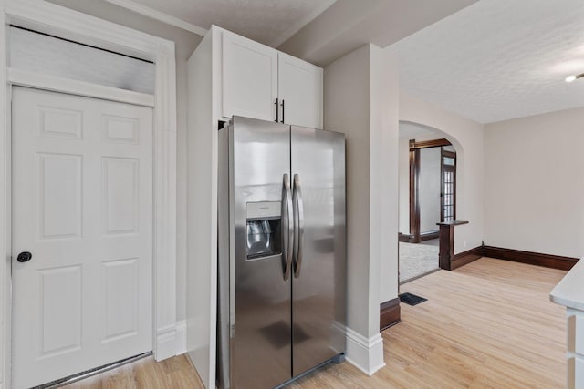 kitchen with arched walkways, white cabinetry, baseboards, stainless steel fridge with ice dispenser, and light wood finished floors