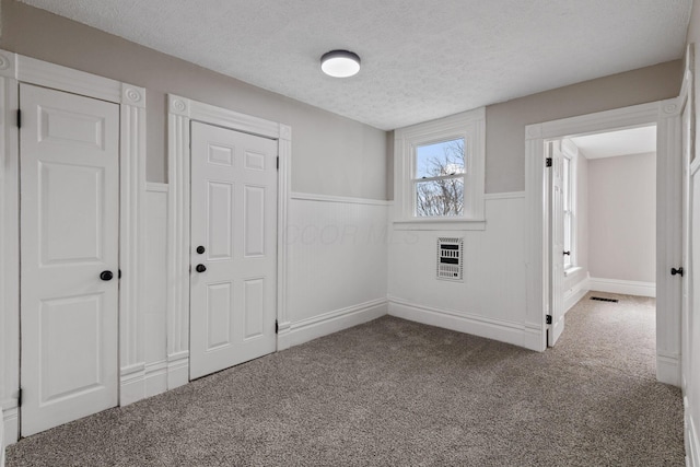 interior space featuring visible vents, a wainscoted wall, a textured ceiling, and heating unit