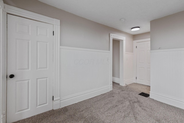 unfurnished bedroom featuring carpet floors, a wainscoted wall, and visible vents