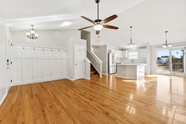 unfurnished living room with a sink, stairs, light wood-style floors, a textured ceiling, and ceiling fan with notable chandelier