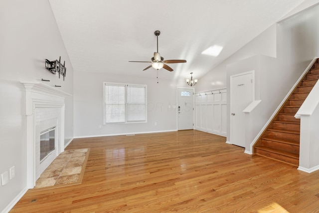 unfurnished living room featuring vaulted ceiling, a fireplace, stairs, and light wood finished floors