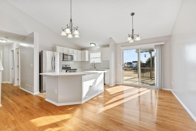 kitchen with light wood-style floors, appliances with stainless steel finishes, white cabinets, an inviting chandelier, and light countertops