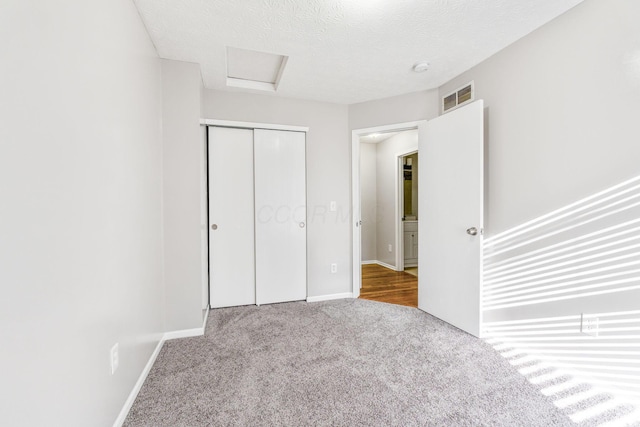 unfurnished bedroom featuring visible vents, a textured ceiling, a closet, carpet floors, and attic access