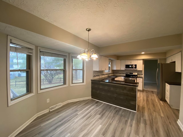 kitchen with dark countertops, visible vents, light wood finished floors, appliances with stainless steel finishes, and a peninsula