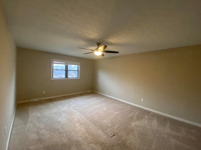 empty room with visible vents, a textured ceiling, carpet floors, baseboards, and ceiling fan