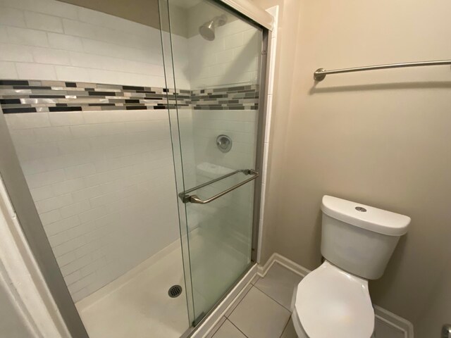 bathroom featuring tile patterned floors, a stall shower, toilet, and baseboards